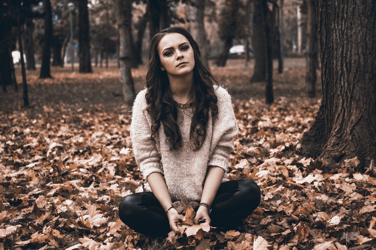 woman in sweater sitting on fallen leaves